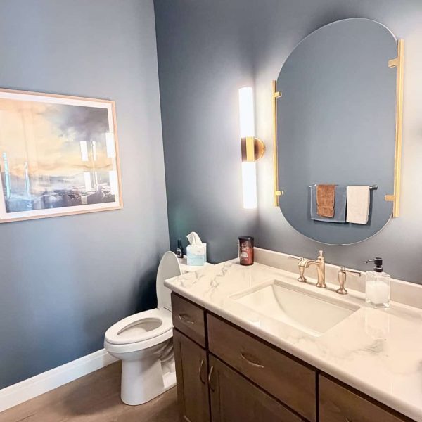 Bathroom with blue walls, white toilet, and wooden vanity with mirror.