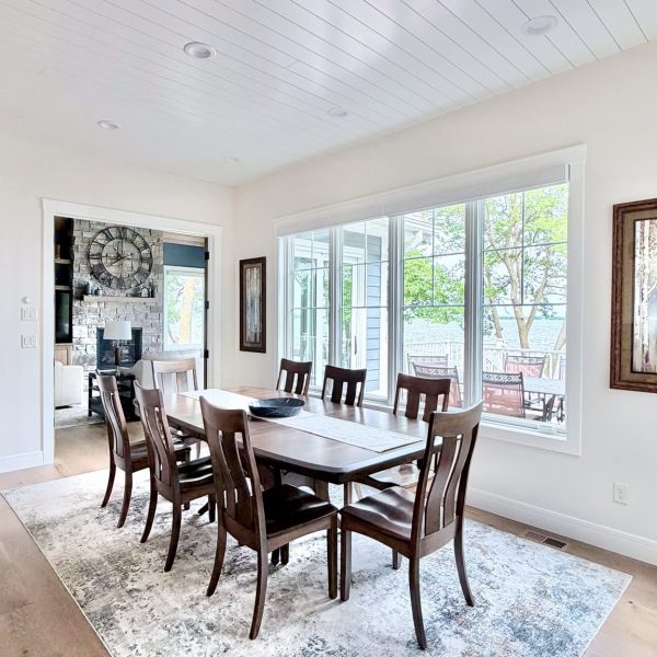Bright dining room with wooden table and six chairs, large windows, and white ceiling.
