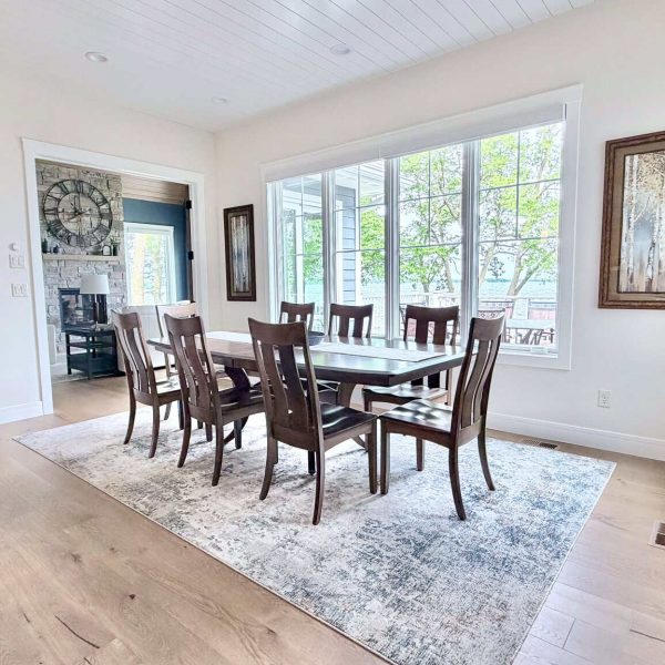 Bright dining room with wooden table and large windows overlooking the outdoors.