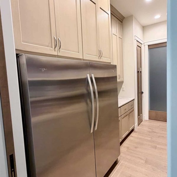 Stainless steel refrigerator in a modern kitchen with beige cabinets.