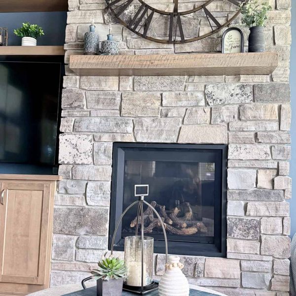 Large rustic wall clock above stone fireplace in living room.