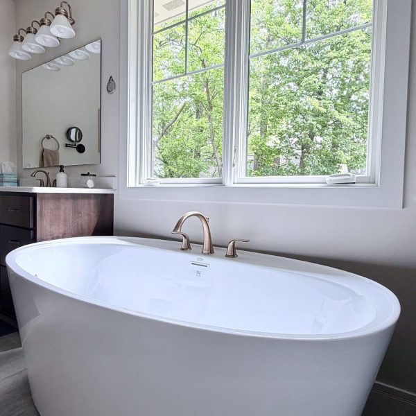 Bright bathroom with large window and white freestanding bathtub.