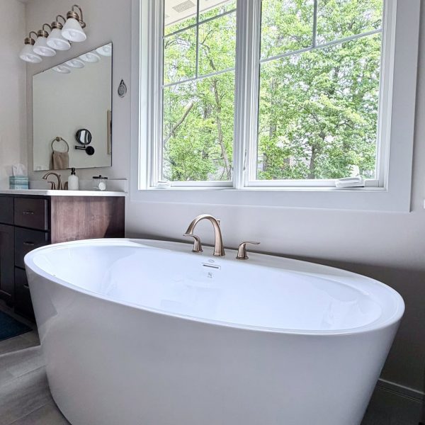 Elegant freestanding bathtub in a bright bathroom with large window and greenery outside.