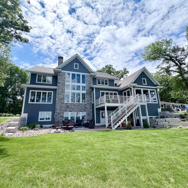 Modern blue house with multiple levels and large windows on a lush green lawn.