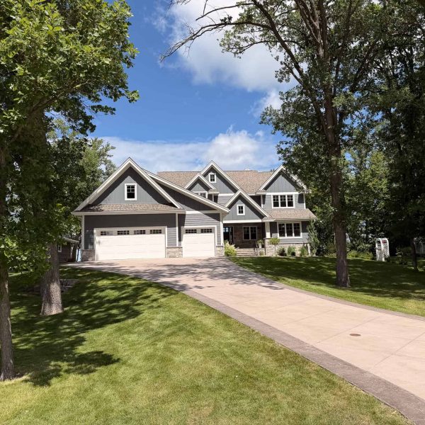 Modern house with large driveway and lush green lawn under blue sky.