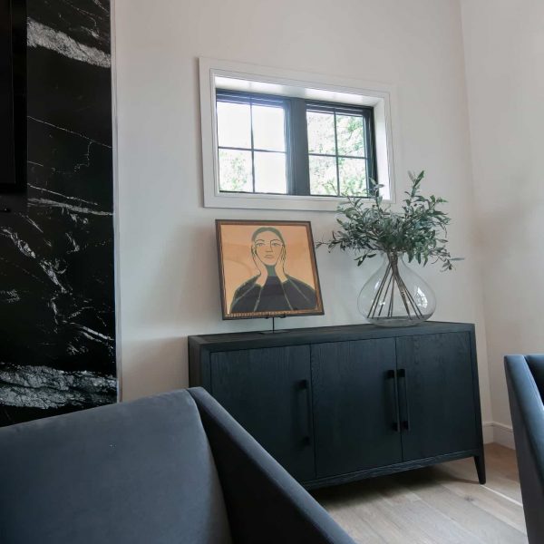 Zunich Home on Detroit Lake living room fireplace sitting area portrait of a woman next to a vase with leafy stems on a black cabinet
