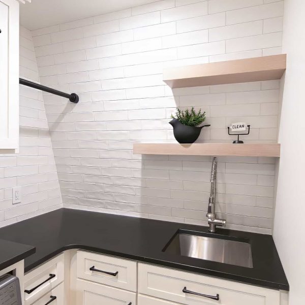 Zunich Home on Detroit Lake Laundry Room sink area with black countertop, white cabinets, and shelving with bird pot with a leafy plant and an iron clean sign