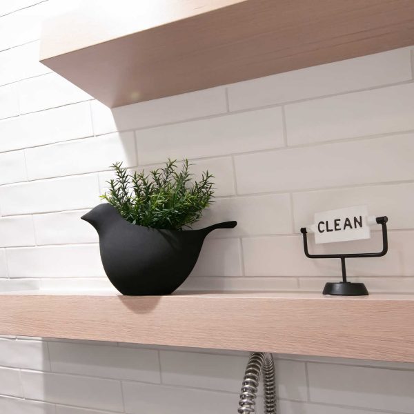 Zunich Home on Detroit Lake Laundry Room black countertop, white cabinets, and shelving with bird pot with a leafy plant and an iron clean sign
